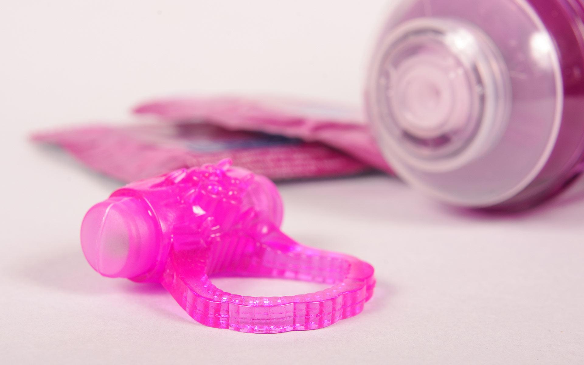 Bright pink cock ring on the ground next to two condoms and a pink tube of lube.