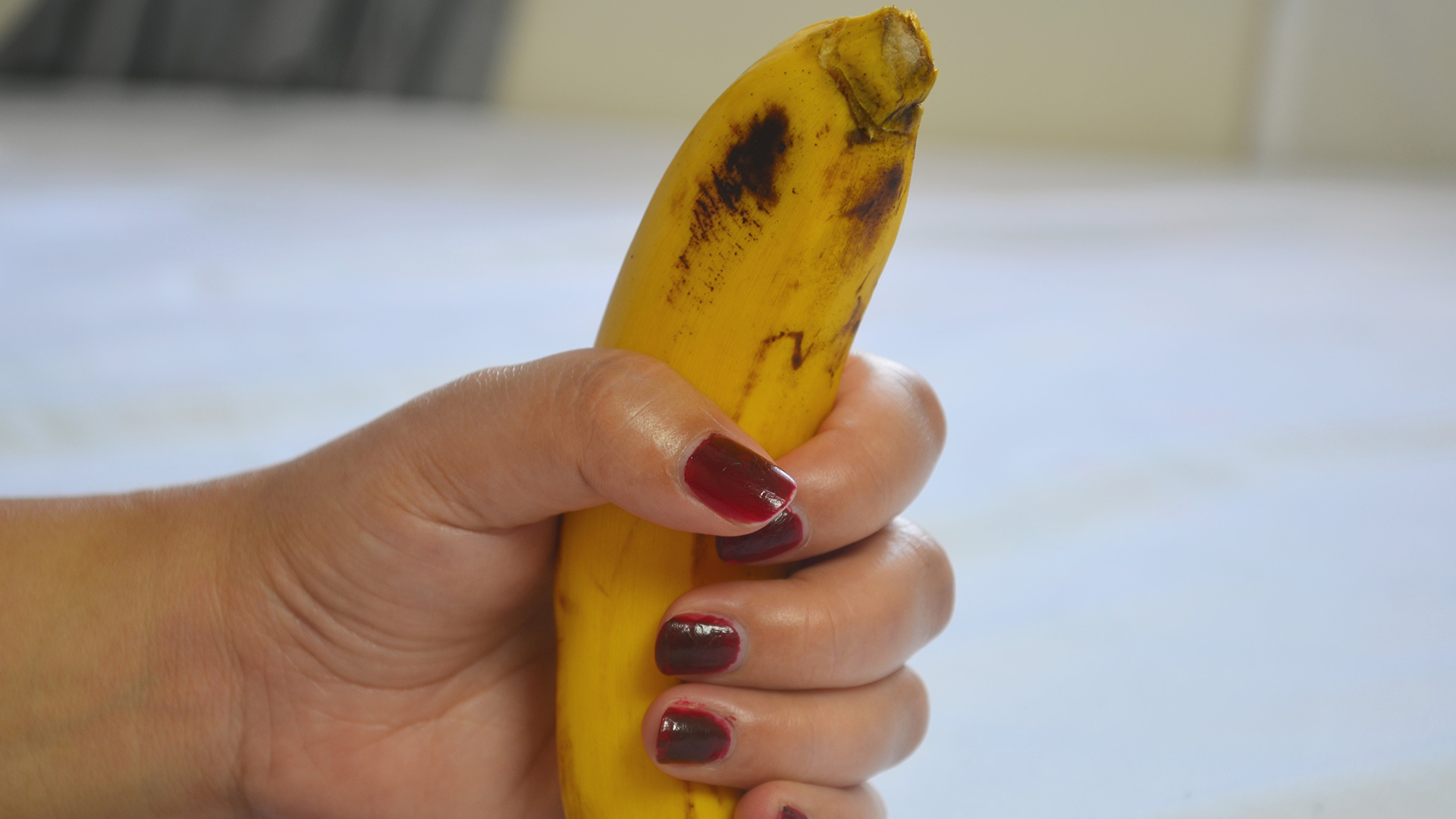 Hand of a woman with red nails gripping a ripe banana.